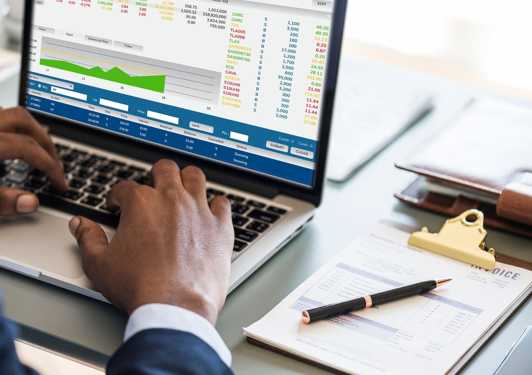 Hands typing on a laptop showing financial data beside an invoice